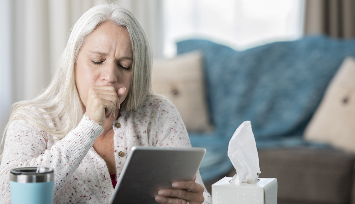 Older woman coughing while holding a tablet