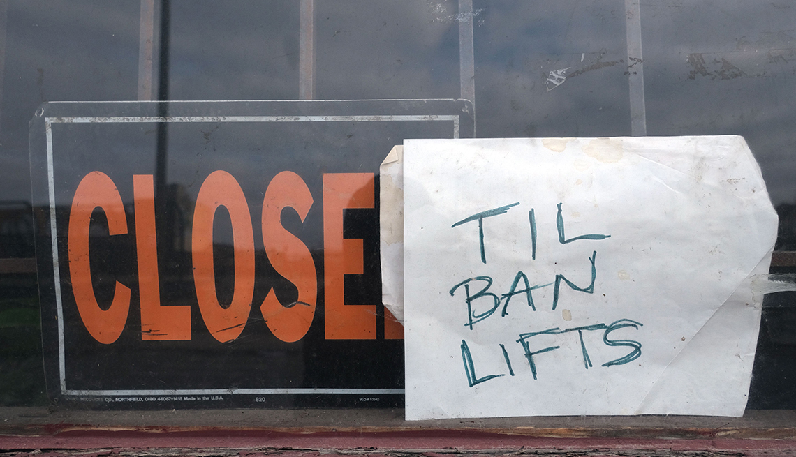 closed sign in the front window of a storefront with a handwritten note added that says til ban lifts referring to the stay at home order imposed by the state