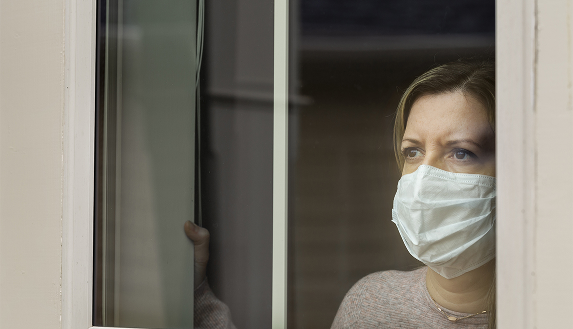 A masked woman in quarantine looks out the window of her home.