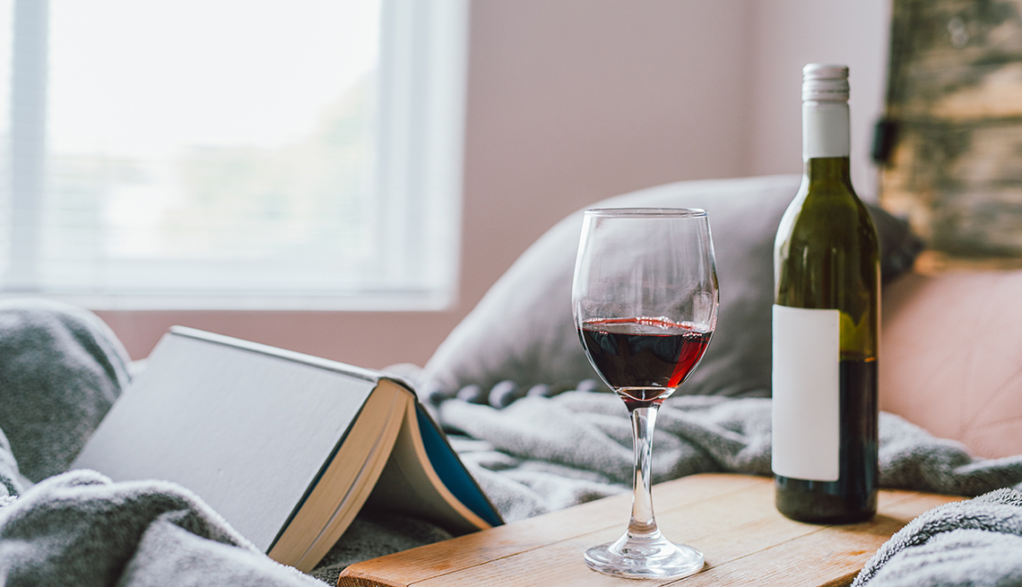 Un libro, una copa de vino y una botella sobre una cama