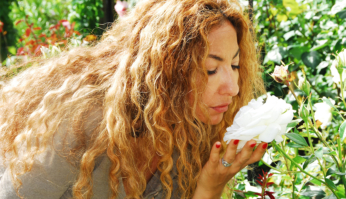 woman bends over to smell a big white flower in a garden