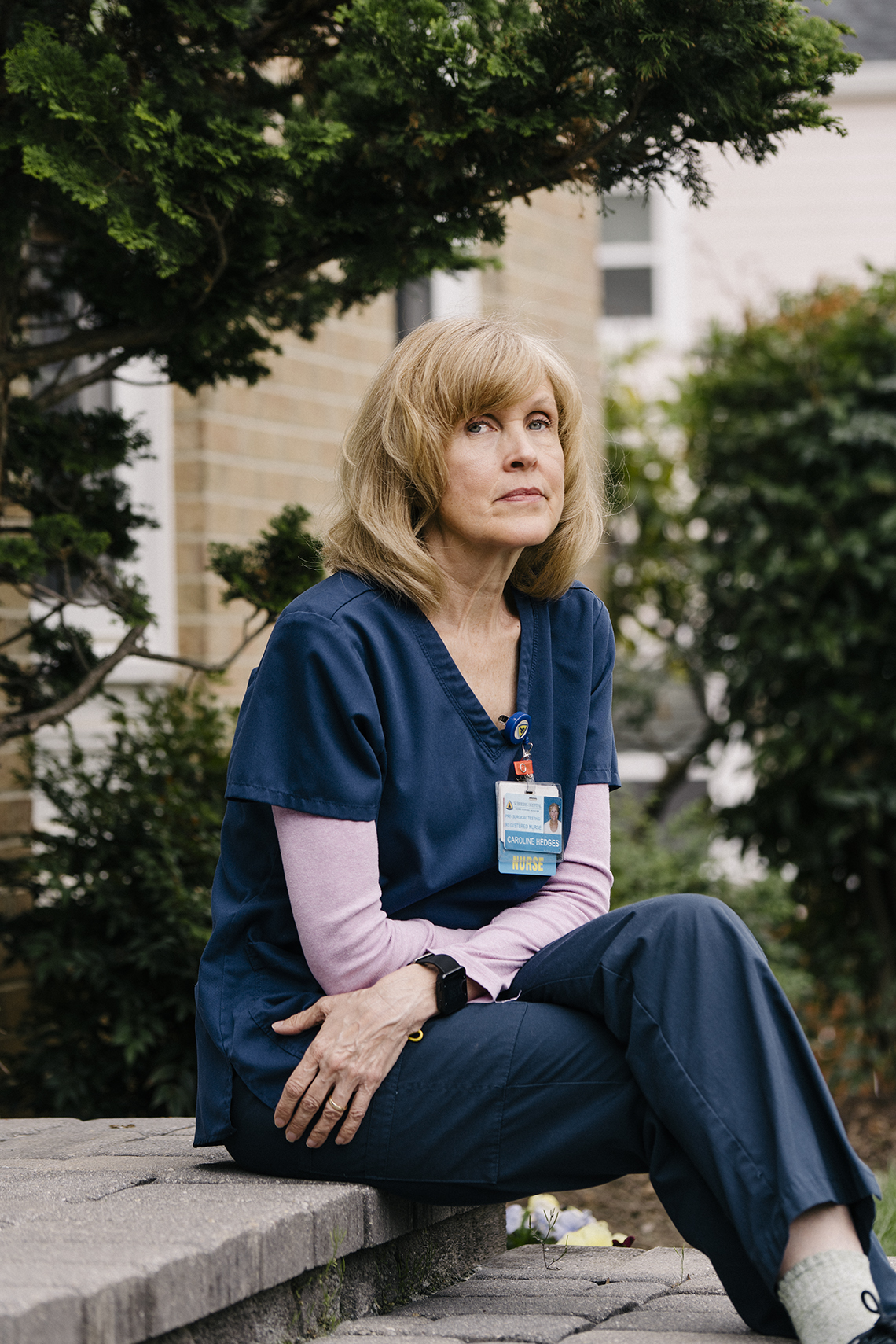 a middle aged nurse sits on the front steps of her building looking pensive