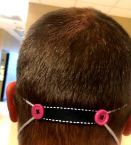 rear head view of a person wearing a buttoned strap to hold their face mask in place instead of looping the straps around their ears