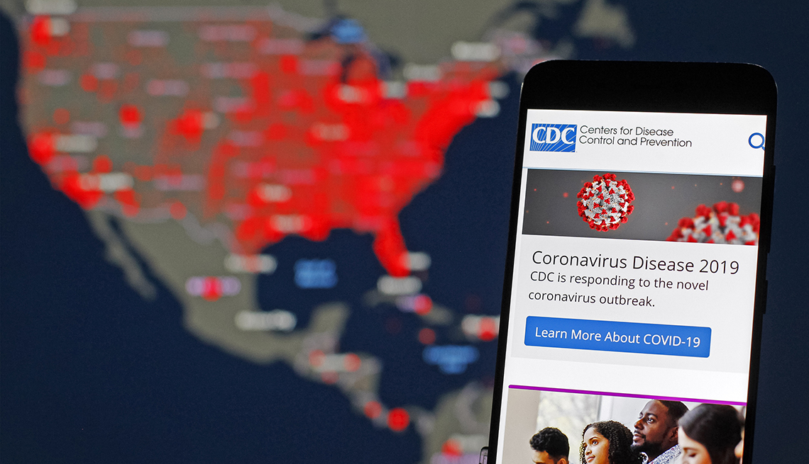 Página web de los CDC desplegada en un teléfono móvil y al fondo un mapa 