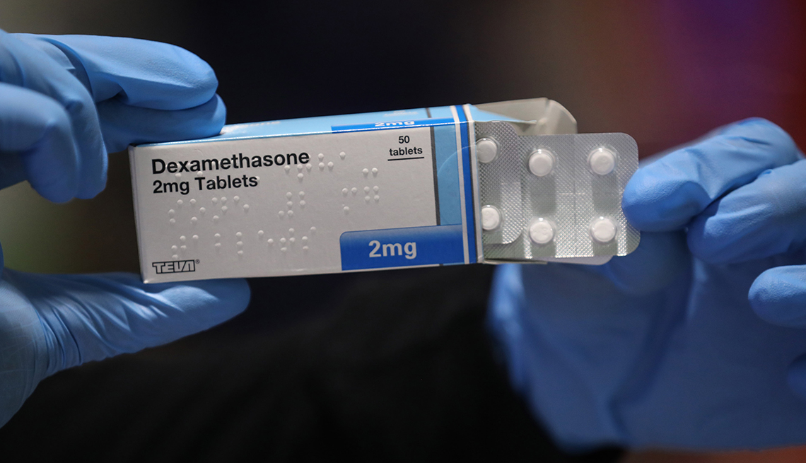 A pharmacist wearing protective latex gloves handles a packet of dexamethasone