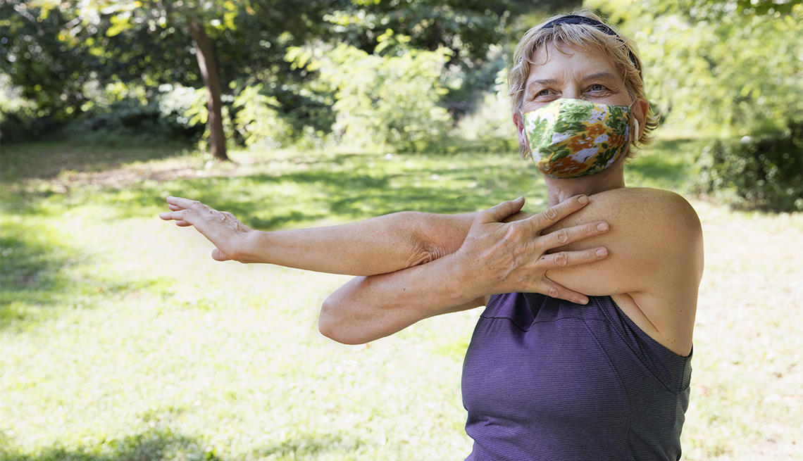 Una mujer hace ejercicio afuera en un parque mientras usa una mascarilla