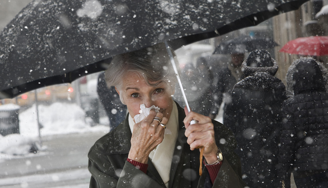 Woman outside in the snow holding an umbrella and blowing her nose.