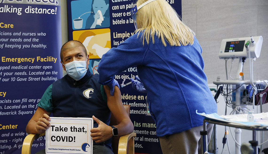 Man getting a covid-19 vaccine, holding a sign that says "Take that COVID!"