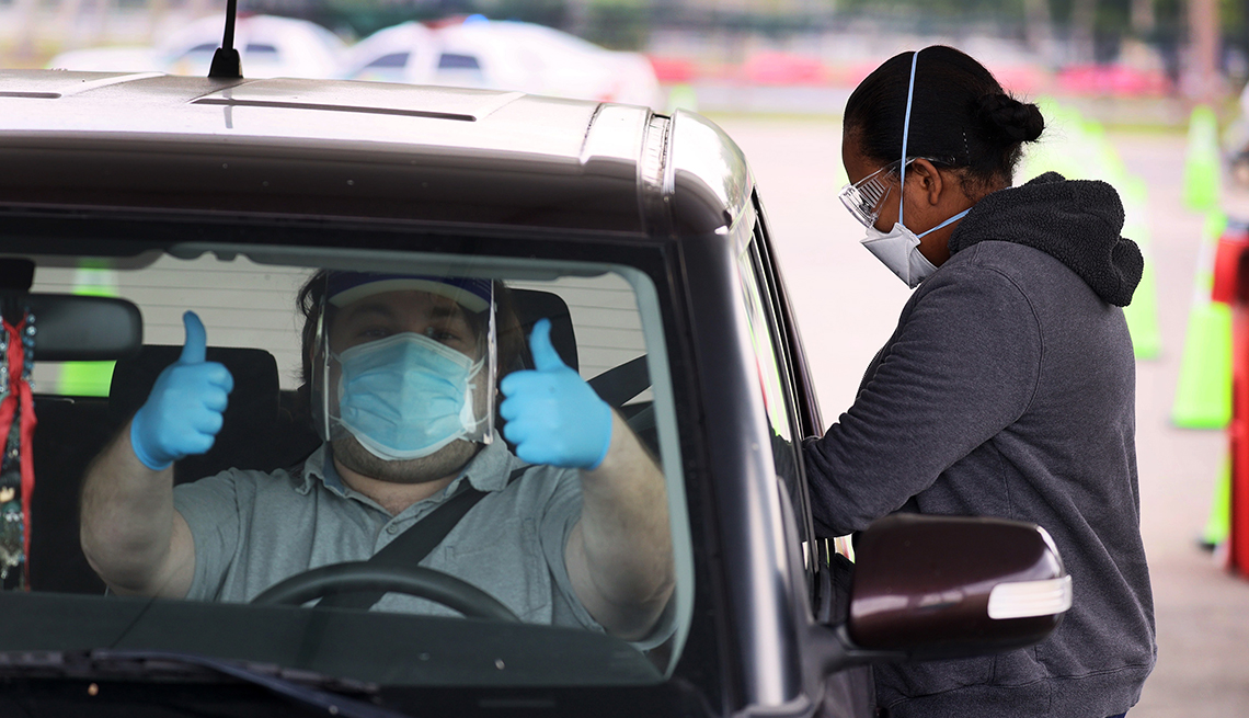 item 6 of Gallery image - a driver in protective gear give a thumbs up from inside his car at the vaccination site in tropical park in miami florida