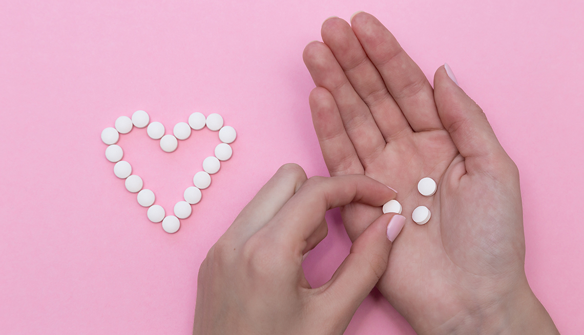 Woman's hand holding white pills next to a heart outline of white pills