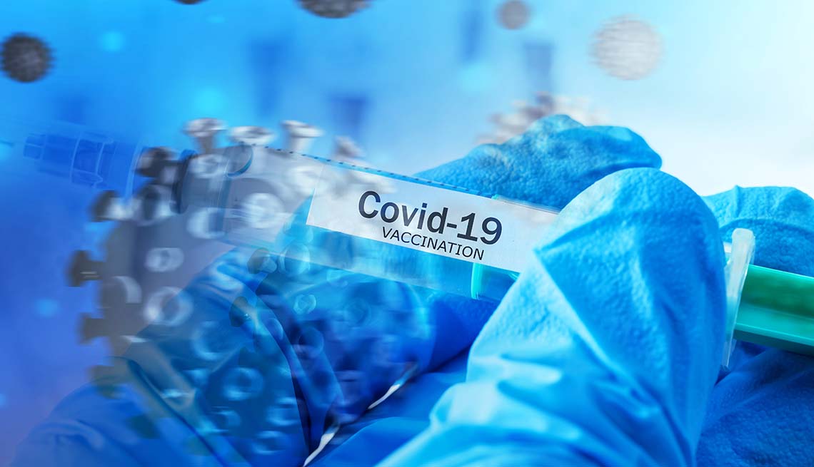 Mano de un médico con guantes azules sostiene una jeringa de la vacuna contra la COVID