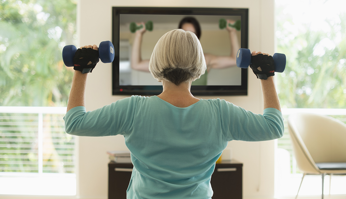 Una mujer hace ejercicios en la sala de su casa mientras ve un video en la TV