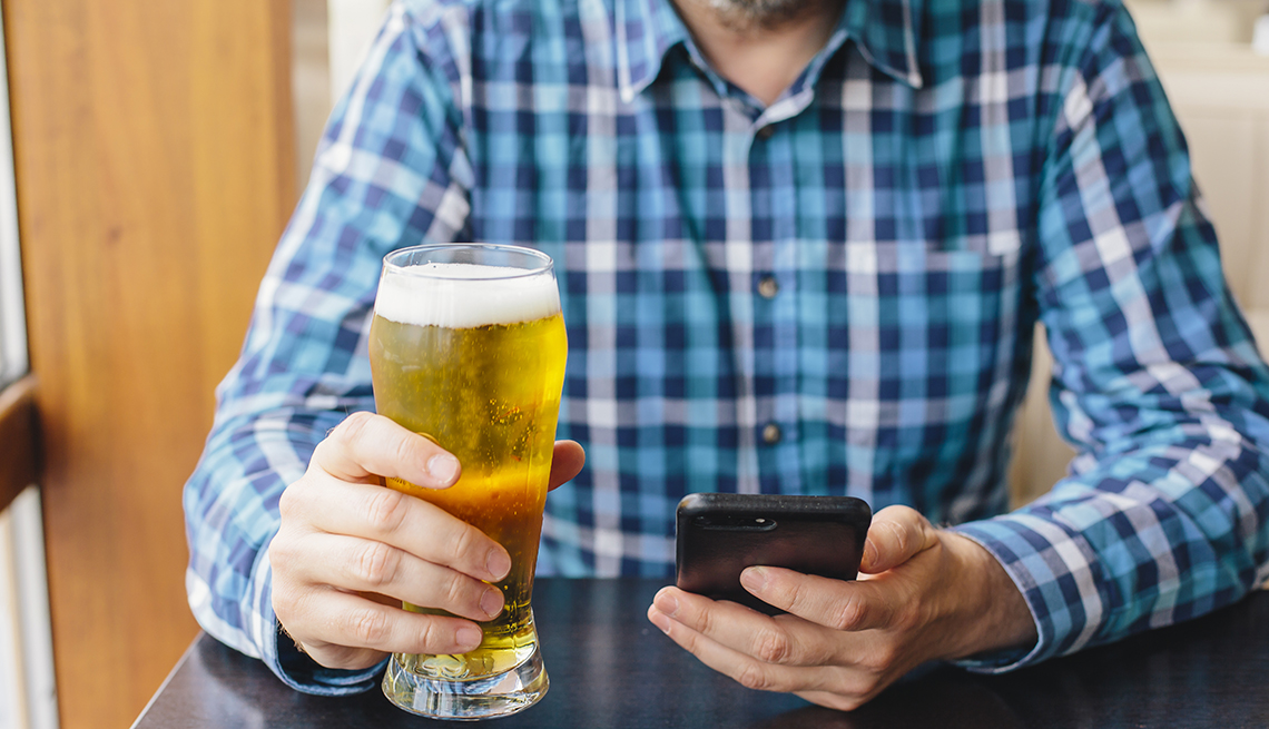 Un hombre con una cerveza en la mano y su celular en la otra