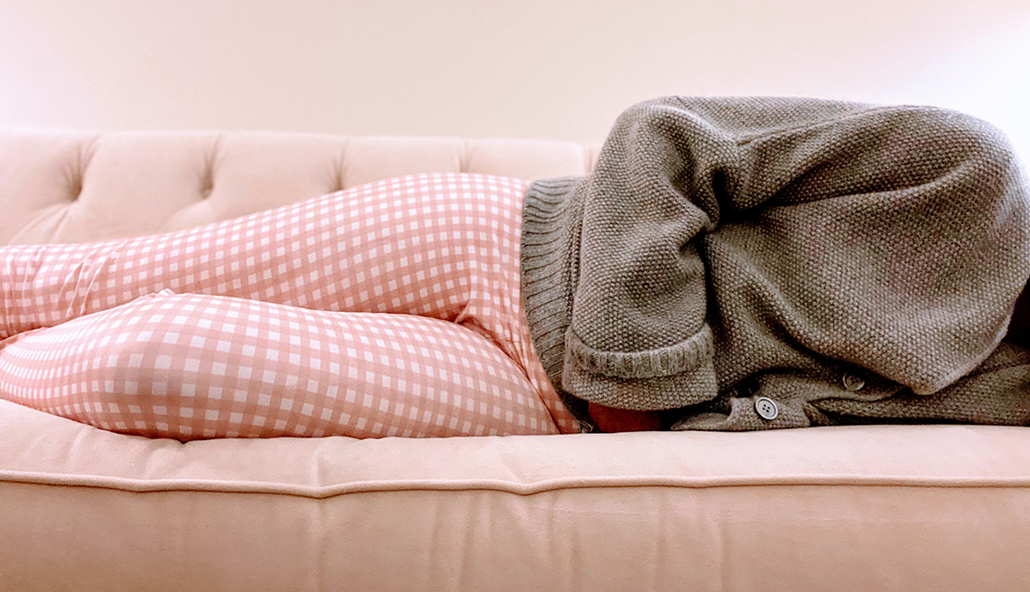 Una mujer acostada en un sofá con sus manos en el estómago en señal de dolor