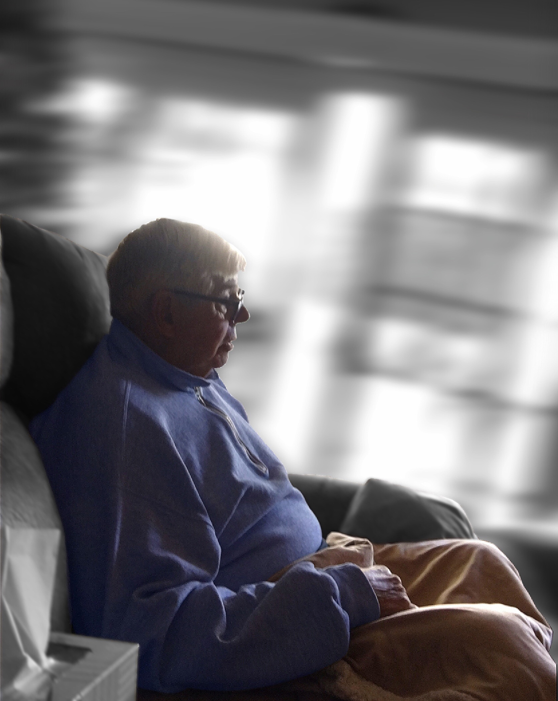 photograph of older man seated in chair with the room around him blurred