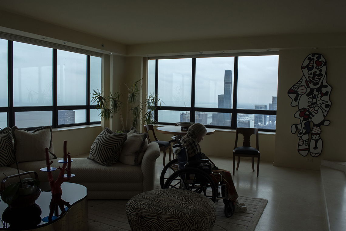portrait of an older woman in a wheelchair in a large room in a high rise building with a view of a city