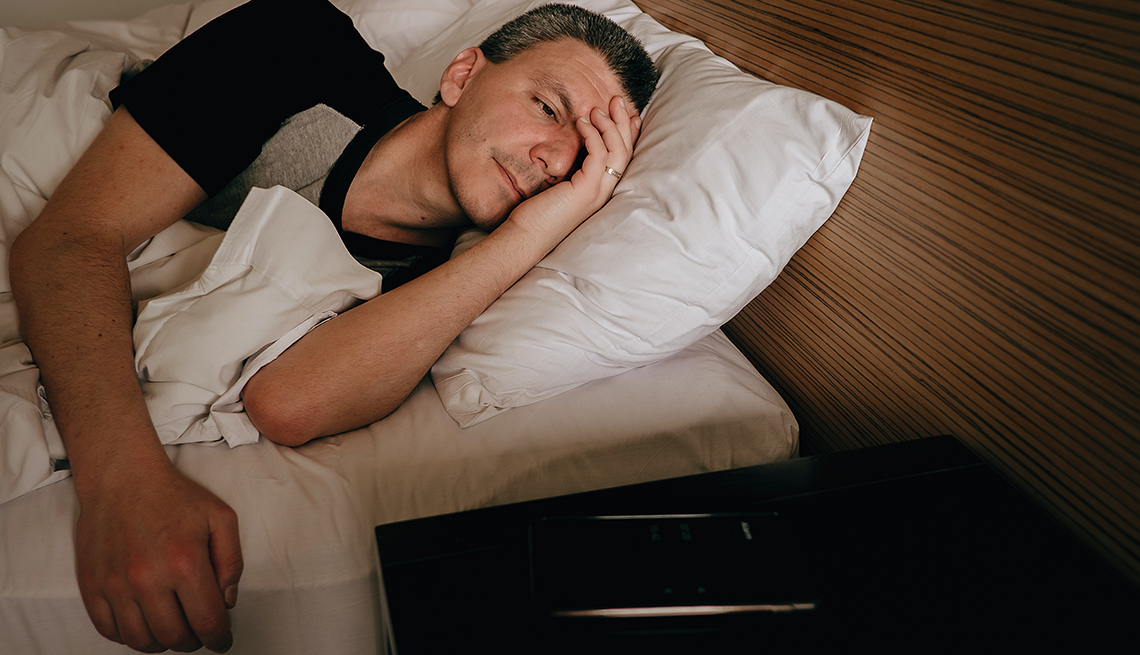man having trouble sleeping, looking at cell phone next to the bed