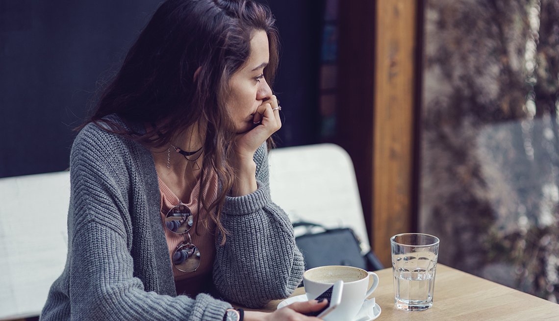 woman having coffee and holding her phone, she looks sad