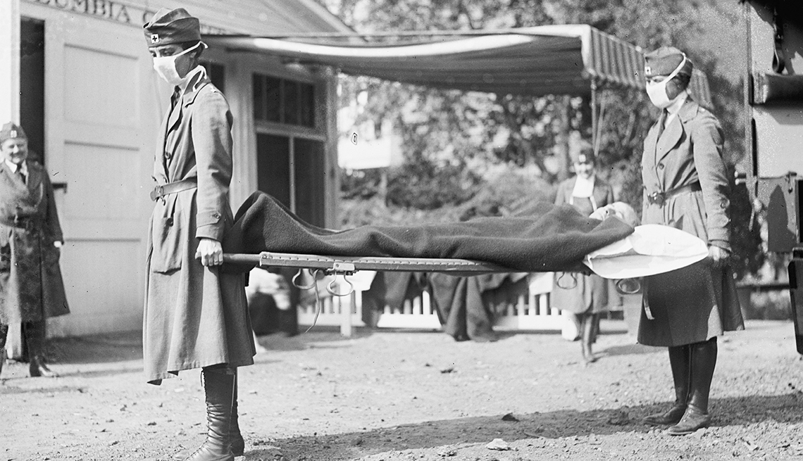 black and white photo from nineteen eighteen showing red cross volunteers doing a demo of how to carry a person on a stretcher