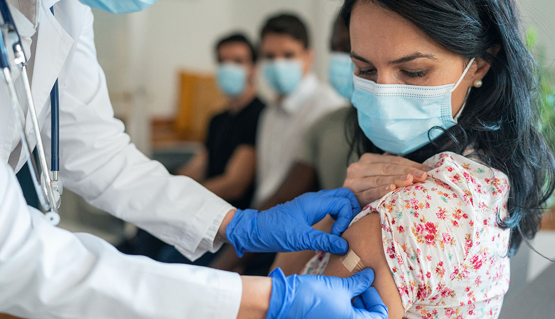 Un doctor coloca una curita donde le puso la vacuna a una mujer