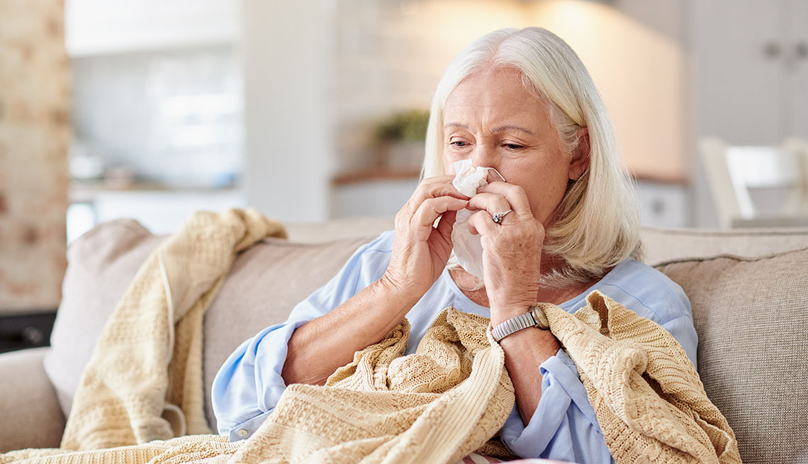 Una mujer sentada en un sofá limpia su nariz con un pañuelo