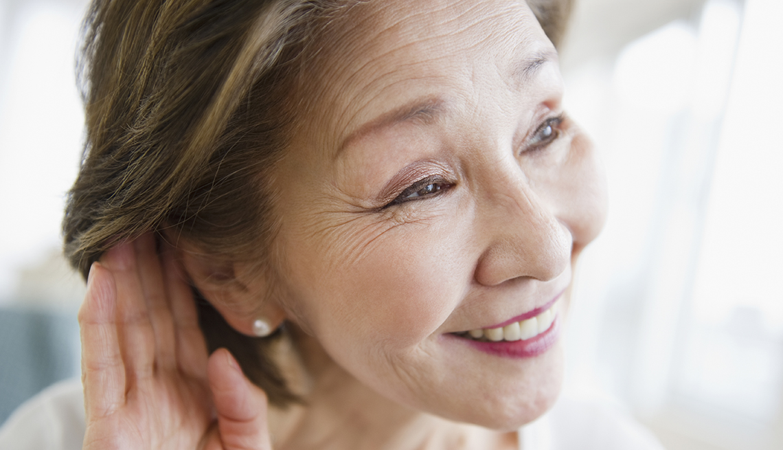 Una mujer pone su mano detras de la oreja para escuchar mejor