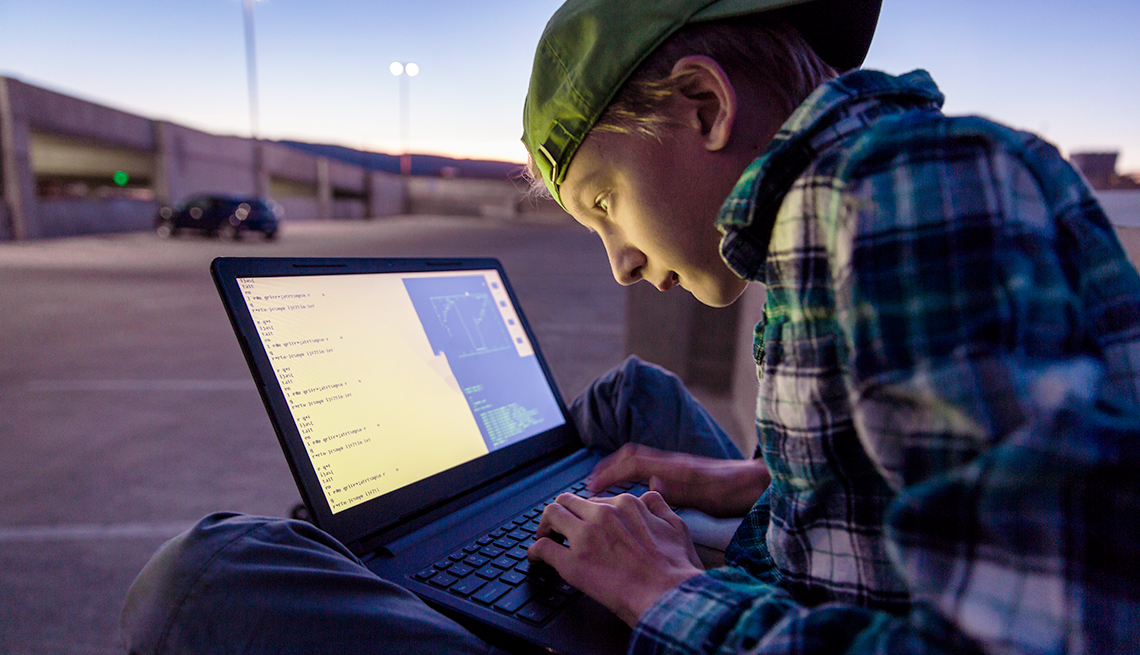 Adolescente sentado y sosteniendo una computadora personal mientras ve su pantalla en un estacionamiento