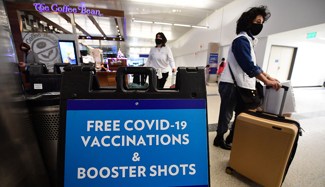 Personas transitan por un aeropuerto donde se ve un letrero que dice vacunas contra la covid gratis