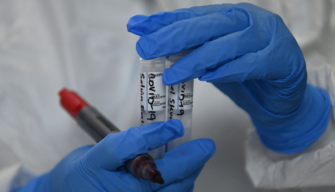 Personal de un laboratorio sostiene unos tubos de ensayo que dicen COVID-19