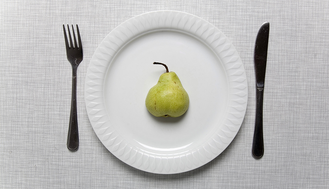 Mitad de una pera en el centro de un plato, cuchillo colocado a la derecha de la mesa y tenedor colocado a la izquierda.