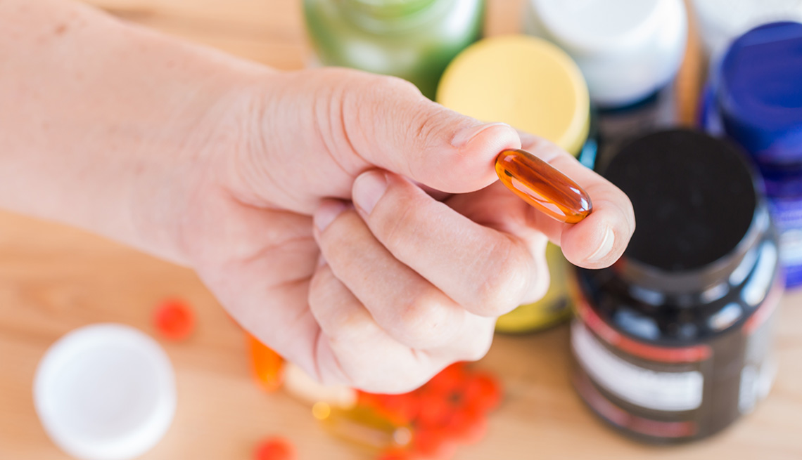 Close-up of a hand holding a vitamin supplement pill. Pill bottles in the background.
