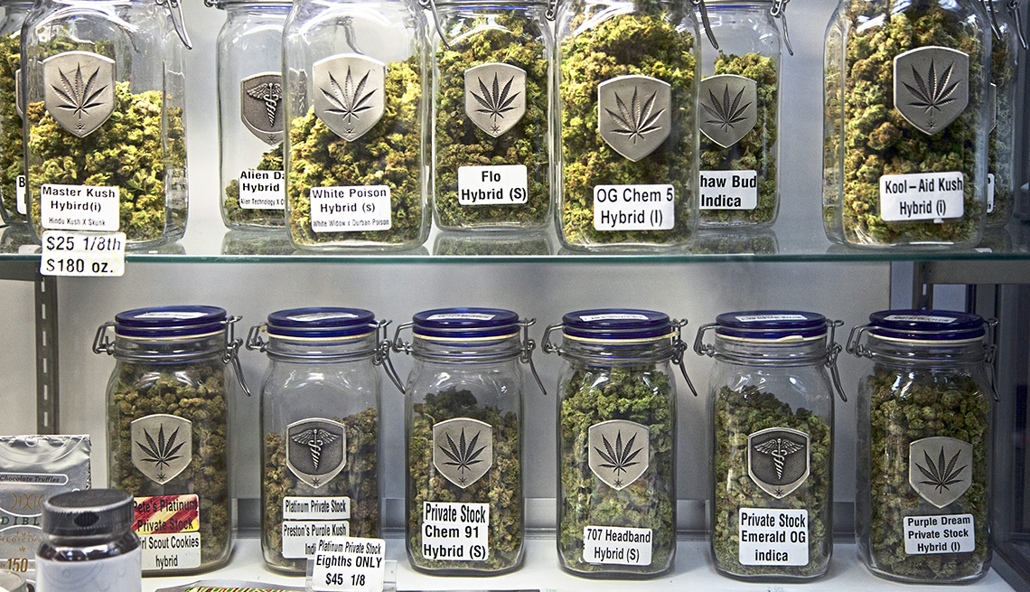 Two shelves holding over a dozen mason-jar-sized labeled glass jars containing marijuana buds of different strains