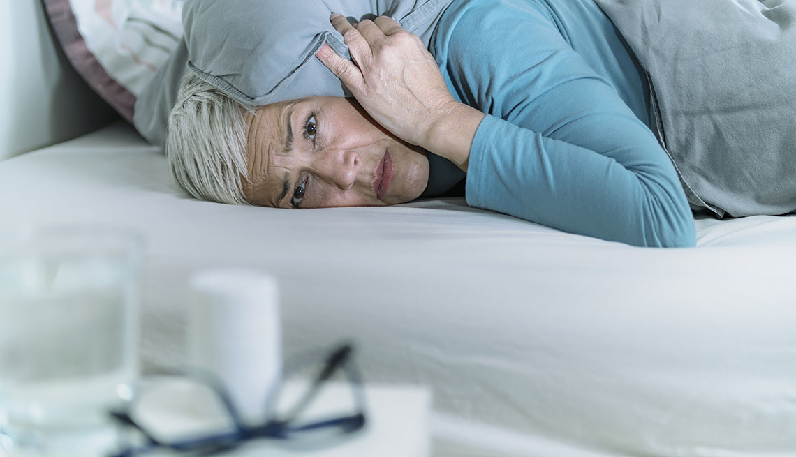 Una mujer acostada, con la almohada sobre su cabeza, sin poder dormir