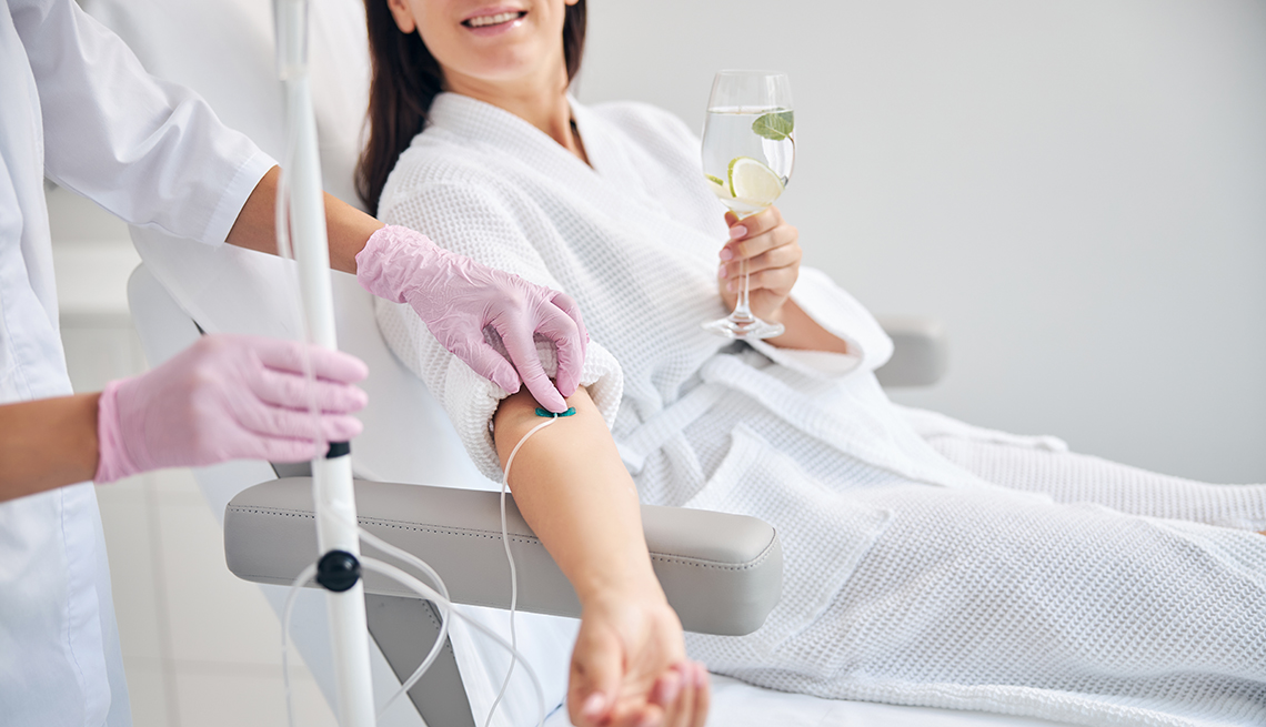 woman holding a water with fruit in it and getting an iv drip placed in her arm at a drip bar