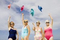 Group of senior women in bathing suits tossing hats in air