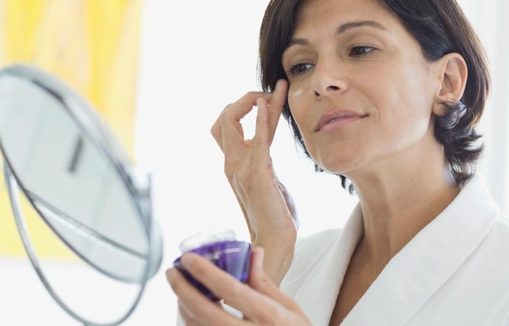 Mujer aplicándose una crema en la cara - Alimentos que protegen tu piel