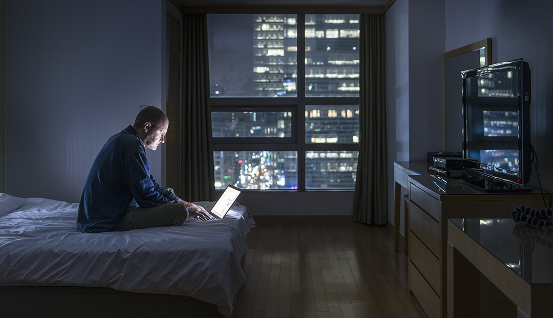 Hombre sentado en su cama con el computador a media noche