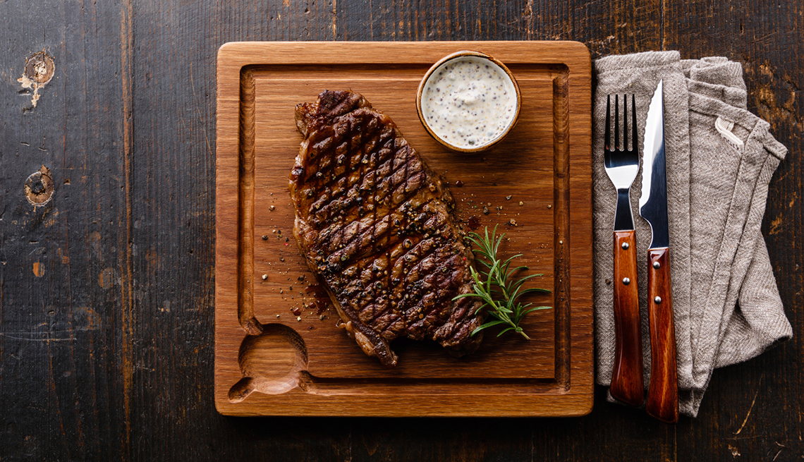Grilled Steak Striploin and Pepper sauce on cutting board on dark wooden background
