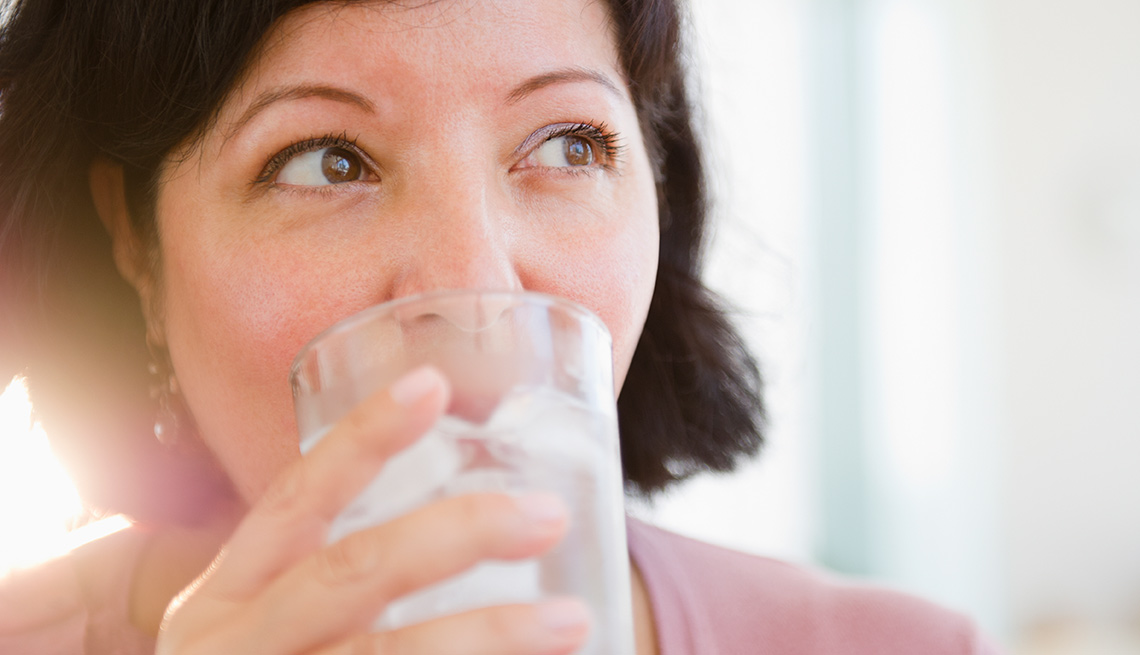 Mujer tomando agua con hielo en un vaso de vidrio - Enfermedades y transtornos que puedes evitar o aliviar tomando agua