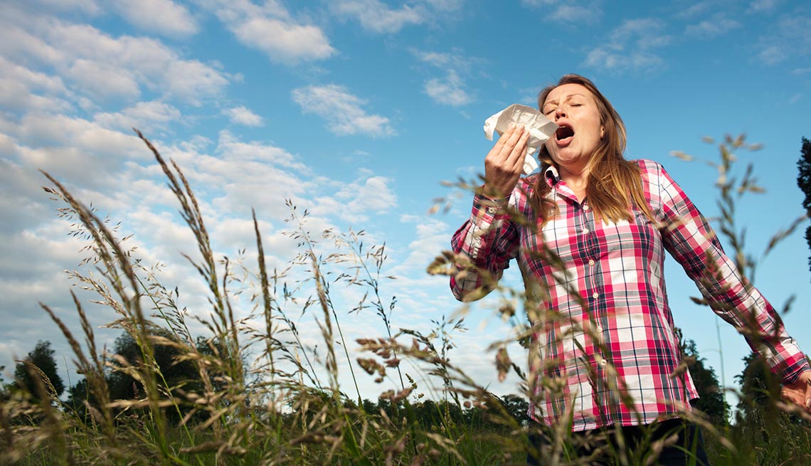 Mujer al aire libre en un campo abierto estornudando - Alergias de temporada
