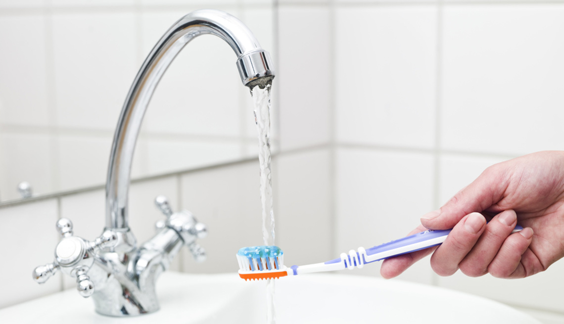 Persona mojando su cepillo dental en el lavamanos