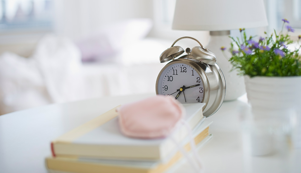Mesa de cama con reloj despertador, libros, lámpara y una planta