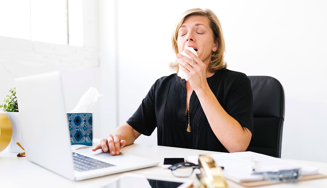 Mature woman sitting at her desk and sneezing 