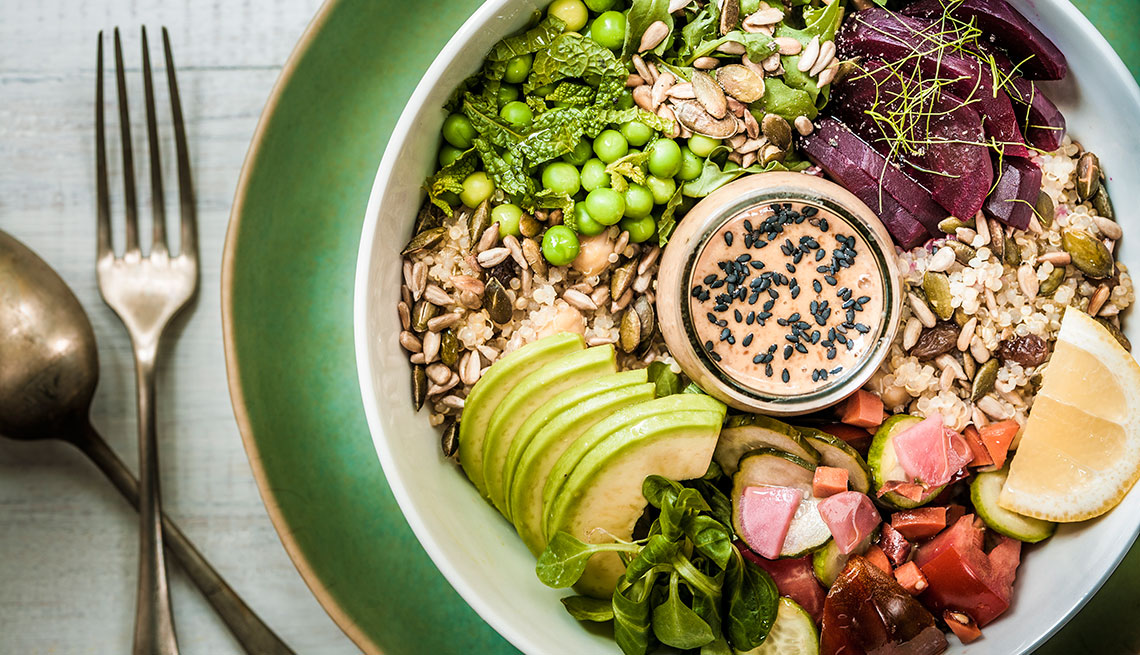 A healthy vegan/vegetarian lunch bowl of salads, grains, seeds, vegetables, avocado slices and a rich peanut-miso sauce.