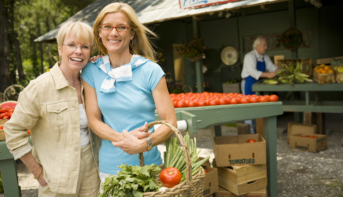 Dos mujeres en el mercado de agricultores con cesta de verduras y tomate.