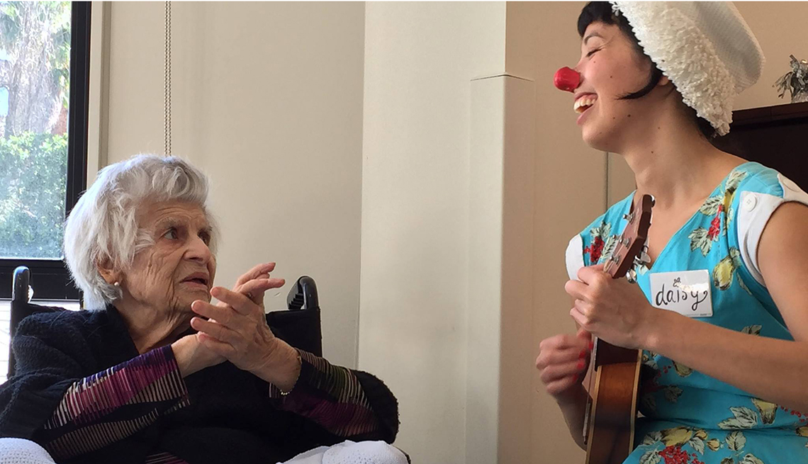 Comedian wearing clown nose and playing music entertains Alzheimer's patient