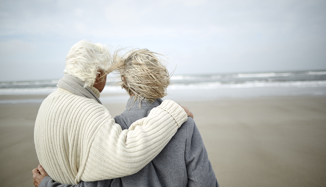 An elder couple embraces while looking at the ocean