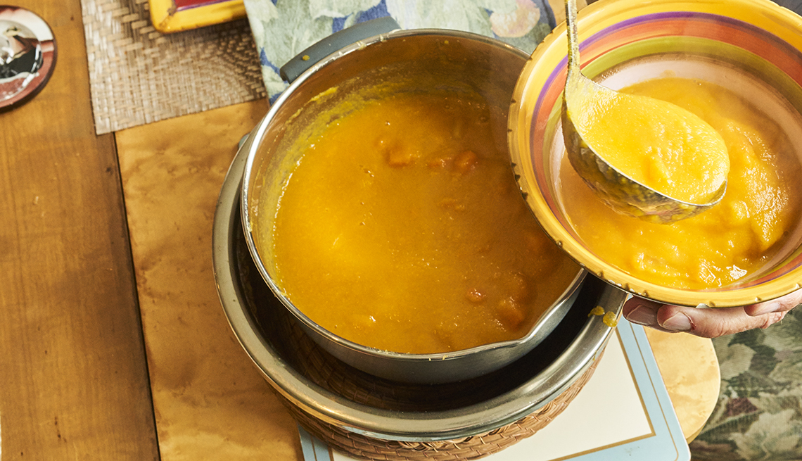 Serving an orange-colored soup into a bowl. 