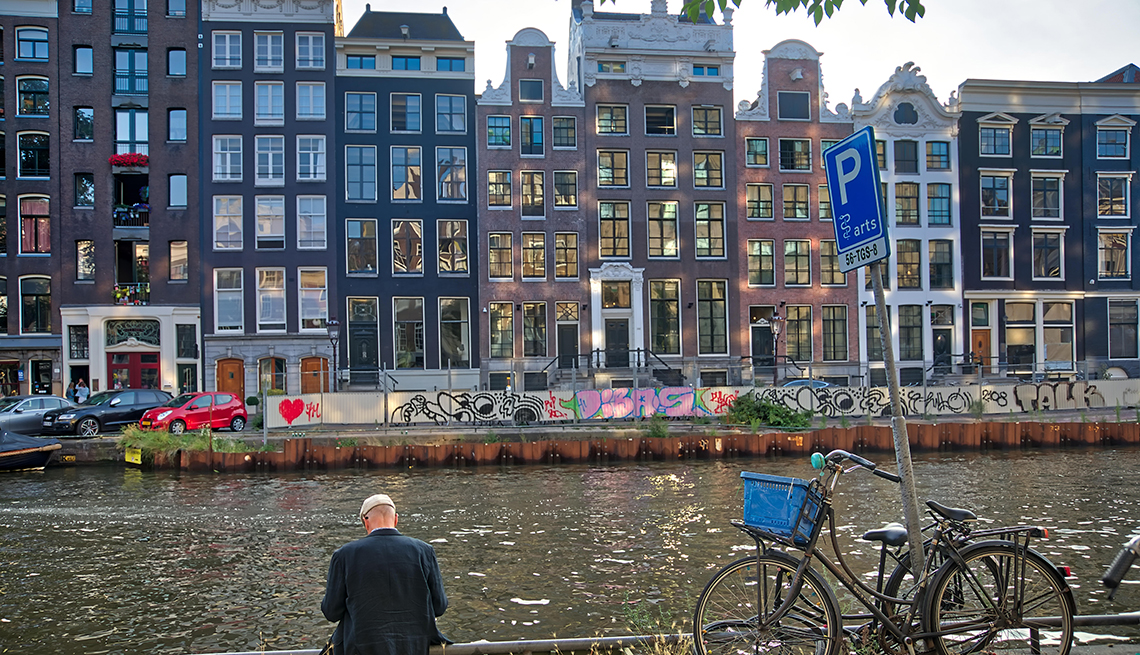 A mature man gazing down at a canal in Amsterdam, Netherland. Background view of typical dutch houses.