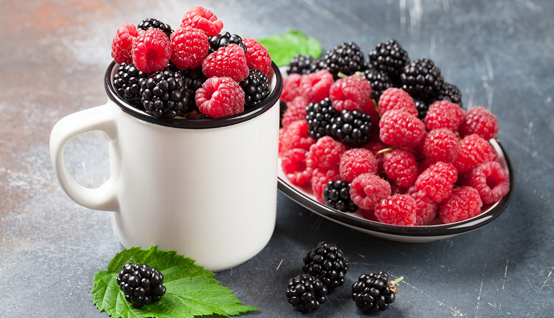 A mix of raspberries and blackberries in a cup and bowl placed next to each other